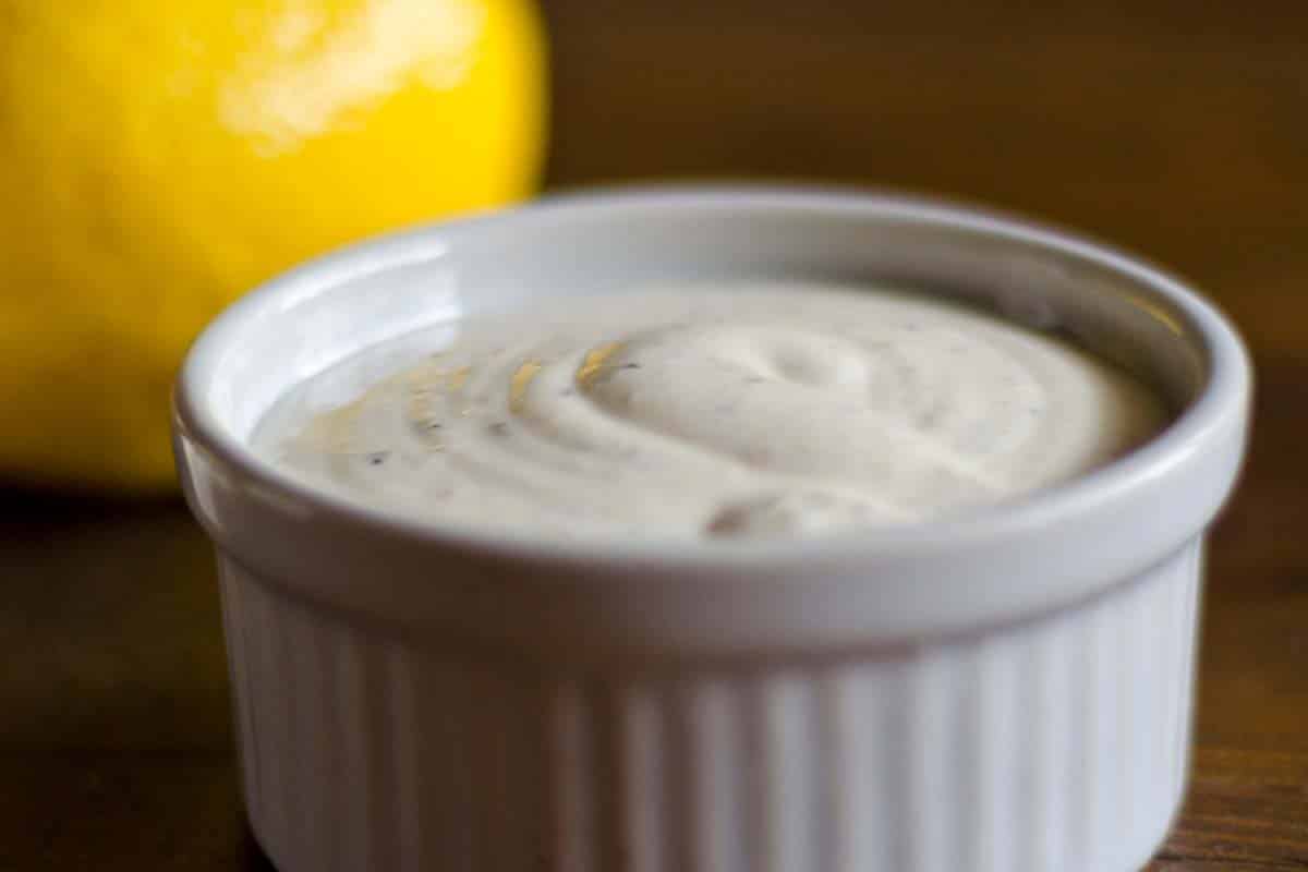 closeup of a ramekin full of homemade Caesar dressing with a lemon in the background