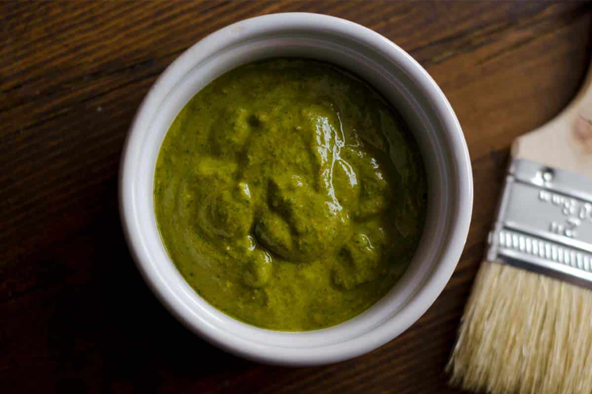 overhead view of a ramekin full of Chermoula wet rub on a wood table with a food brush