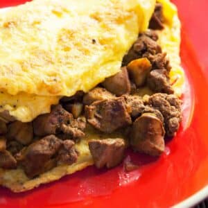 closeup of a red plate holding a large Chicken liver omelet