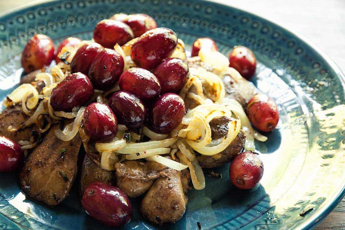 closeup of a blue plate filled with Chicken livers with grapes and onions