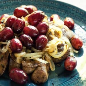 closeup of a serving of Chicken livers with grapes and onions on a blue plate