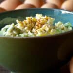 sideview of a bowl of Classic egg salad in front of raw brown eggs