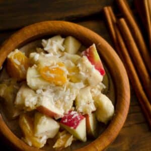 overhead view of Coconut fruit bowl in a wood bowl next to cinnamon sticks on a table