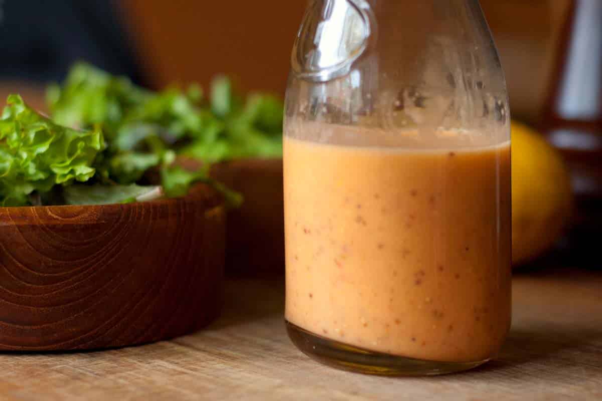 closeup of a glass carafe filled with Crushed tomato vinaigrette on a table with a salad in the background