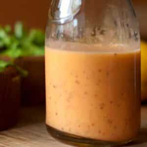 closeup of a glass carafe of Crushed tomato vinaigrette with a bowl of salad in the background