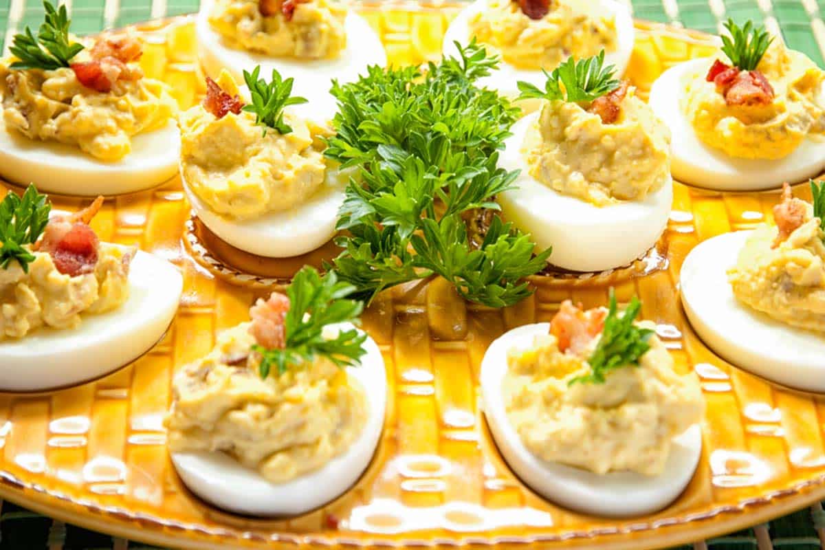 several Deviled eggs with bacon bits on a yellow egg tray’s  with parsley for garnish