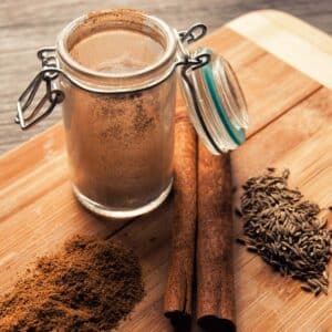 wood cutting board with open jar of homemade Garam Masala with component spices on the board next to the jar