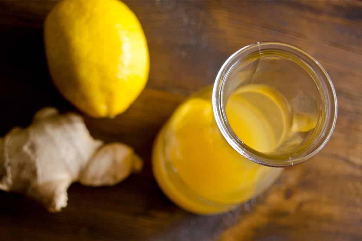 overhead view of Ginger Asian vinaigrette in a glass carafe with a lemon and garlic on a wood table in the backgound