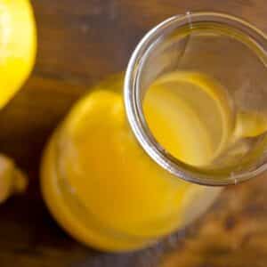 overhead view of a glass carafe of Ginger Asian vinaigrette on a wood table beside a lemon