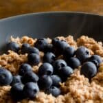 closeup of Grain-free oatmeal topped with blueberries in a grey bowl