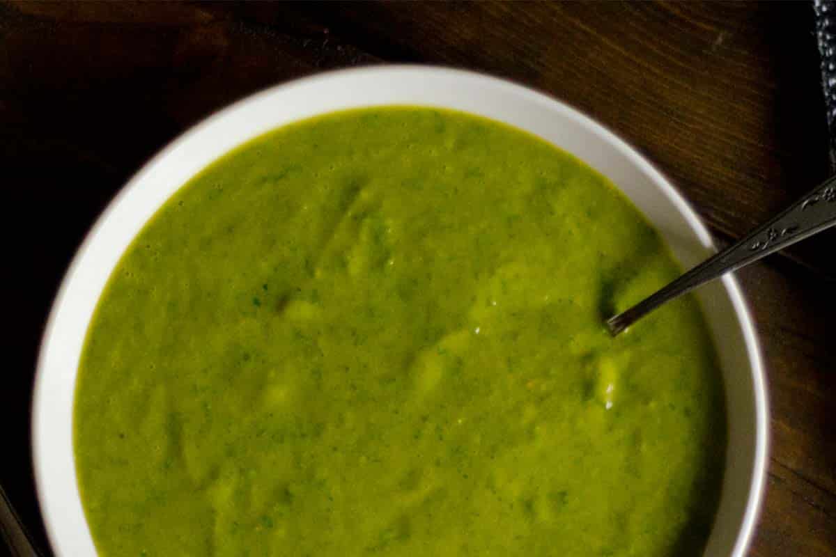 closeup of Green spinach and chard soup served in a white bowl on a wood table