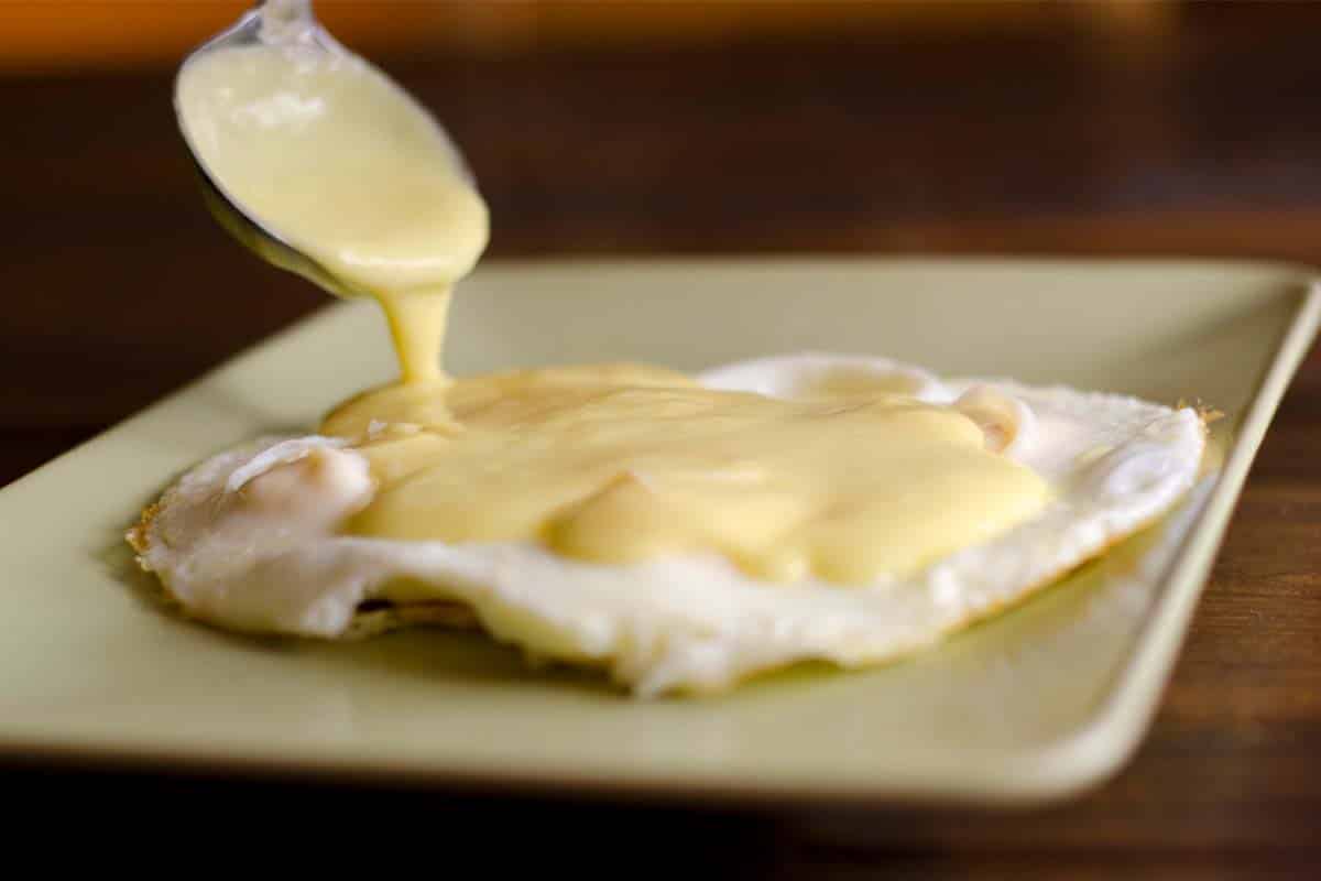 spooning Hollandaise sauce onto a fried egg