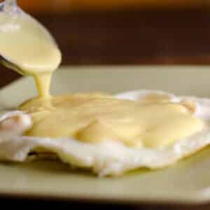 creamy homemade Hollandaise sauce being spooned onto a fried egg