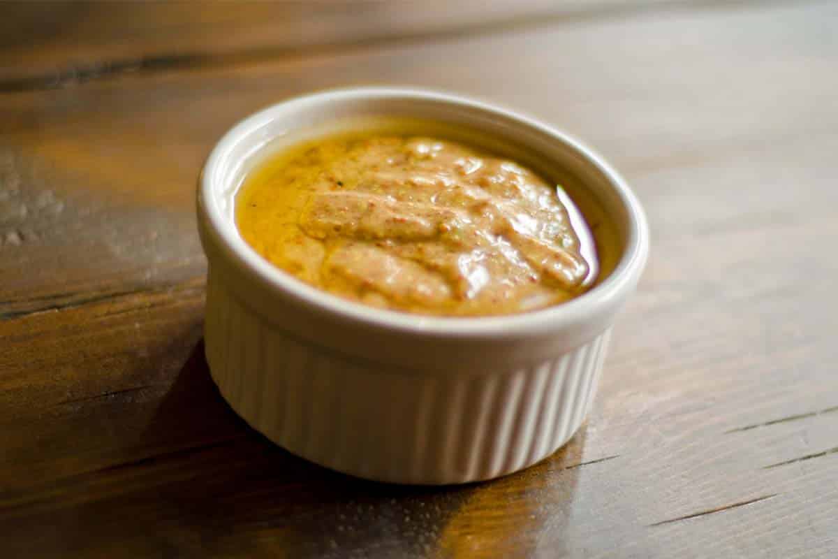 closeup of Honey mustard vinaigrette in a white ramekin on a wood table