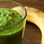 closeup of a glass of Kale and banana green smoothie with a banana in the background