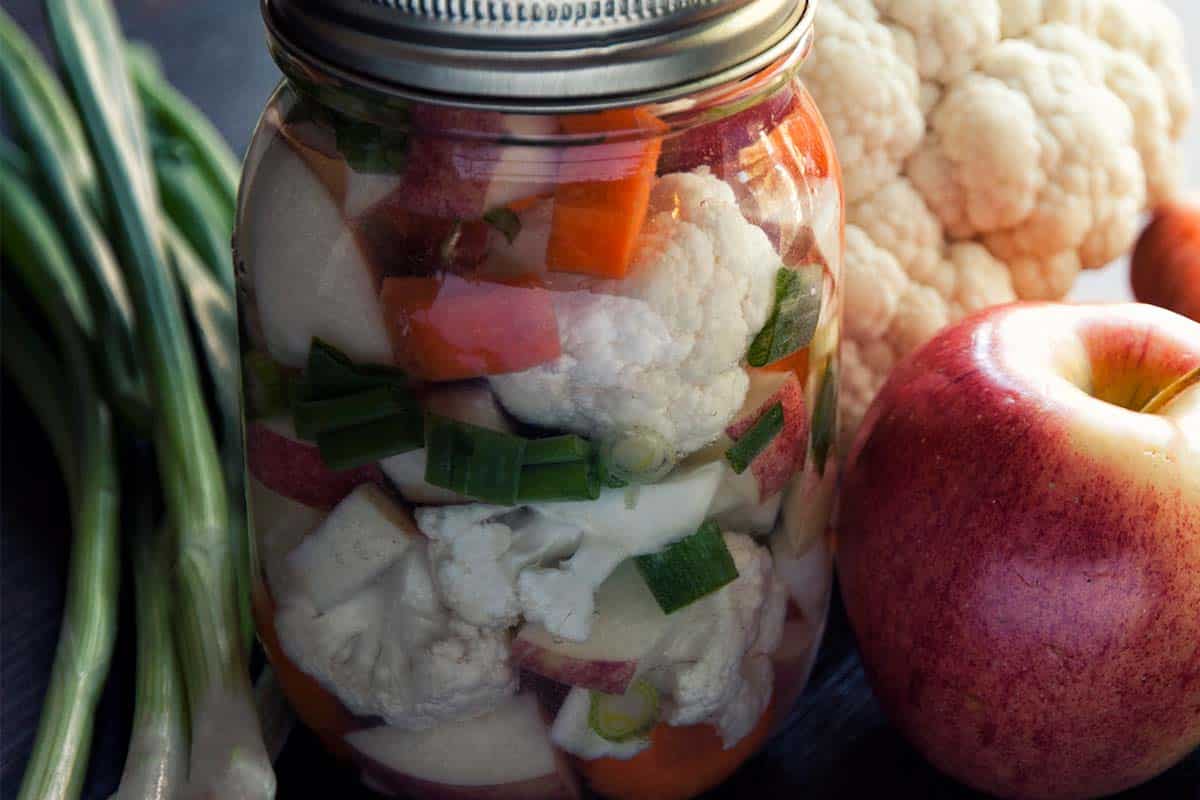 closeup of a jar of Lacto-Fermented Vegetable Medley with raw veggies surrounding