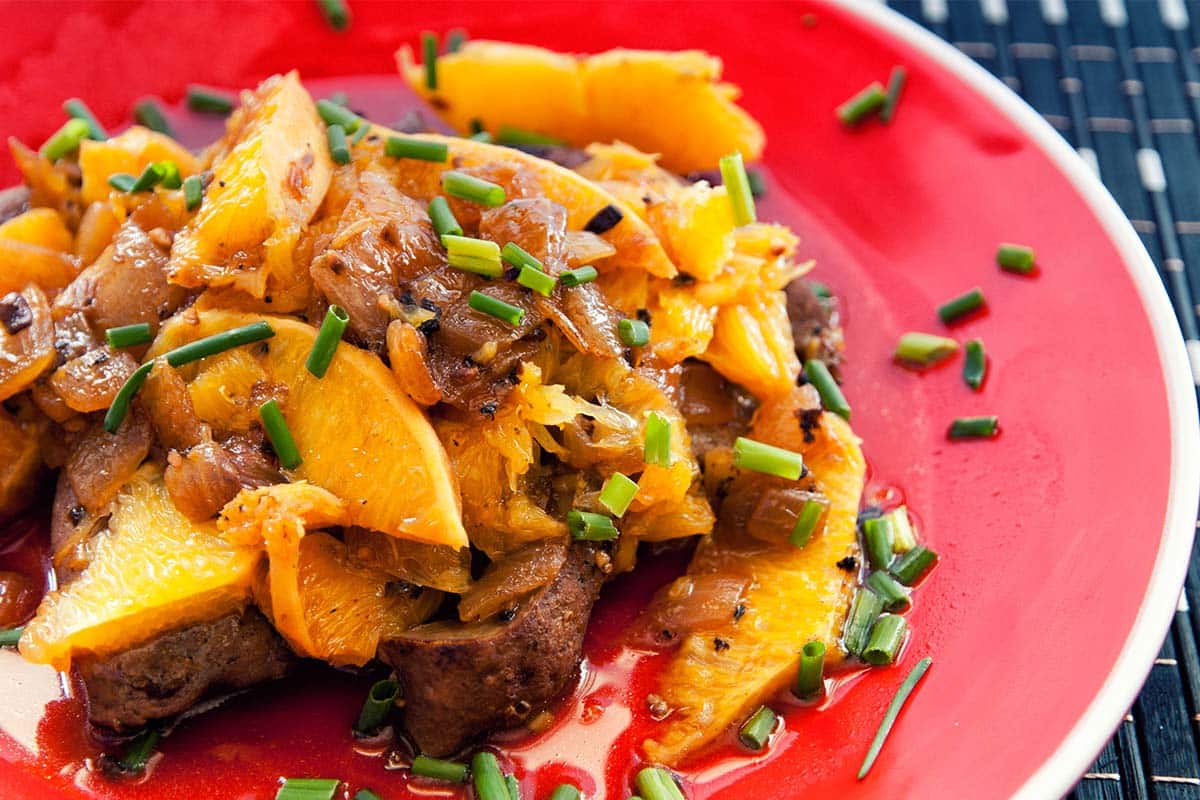 closeup of serving of Lamb Liver with Oranges on a red plate 