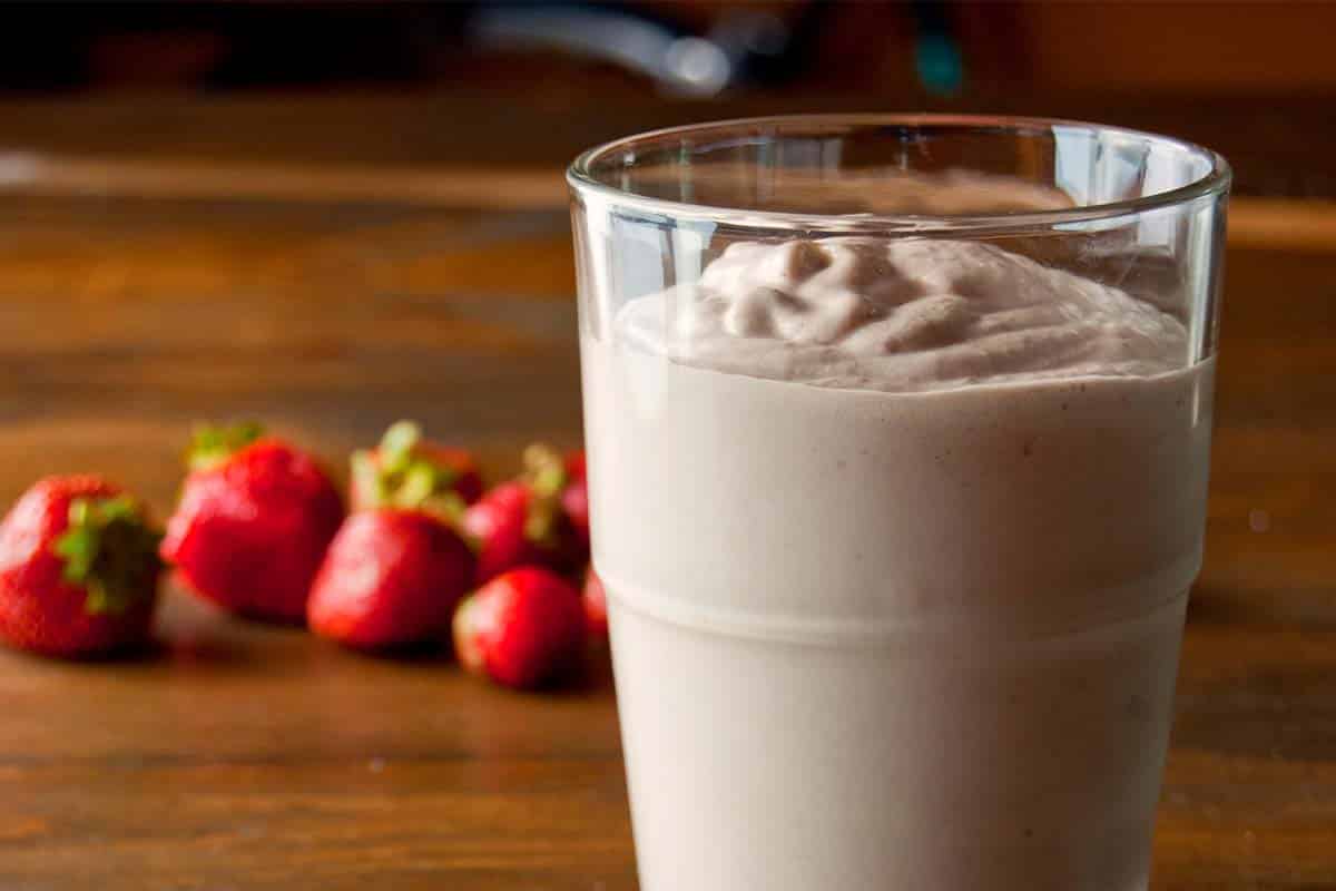 closeup of Macadamia and avocado smoothie in a glass on a wood table with strawberries in the background