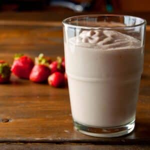 Macadamia and avocado smoothie in a glass on a wood table with strawberries