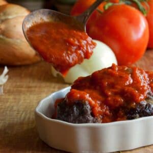 Marinara sauce being spooned on top of meatballs in a white ramekin dish