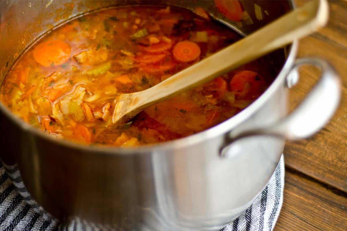 closeup of Minestrone Soup in a large silver pot with a wood spoon