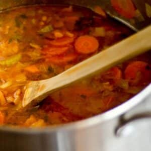 closeup of a silver pot filled with Minestrone Soup with a wood spoon