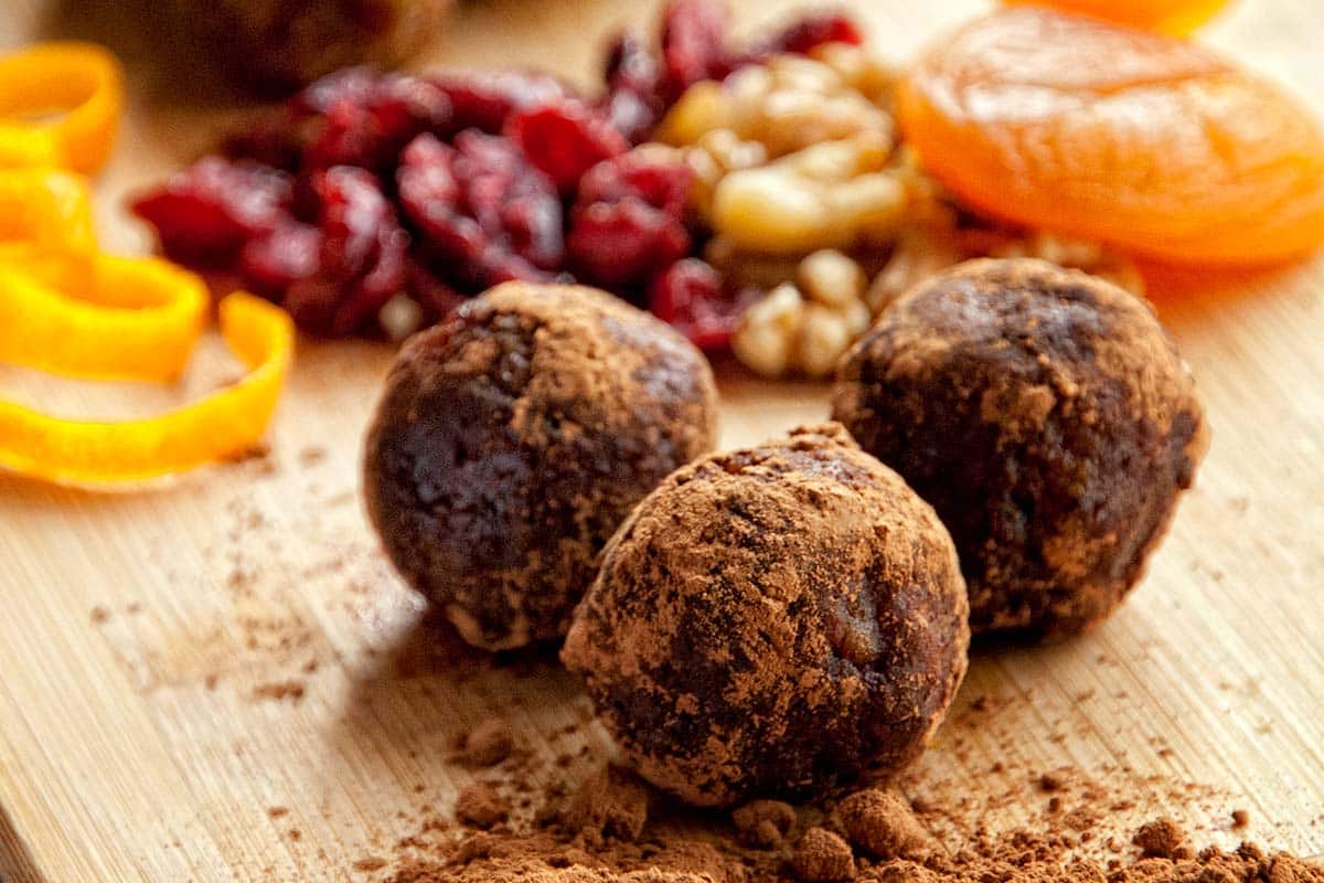 closeup of Nut and fruit balls on a wood serving platter with mixed dried fruit in the backgound