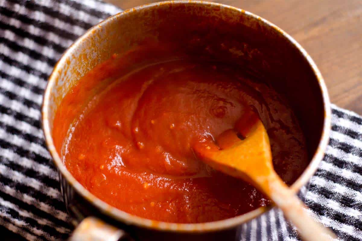 Orange flavored BBQ sauce in a saucepan with a wooden spoon