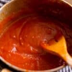 closeup of a saucepan with homemade Orange flavored BBQ sauce being stirred by a wood spoon