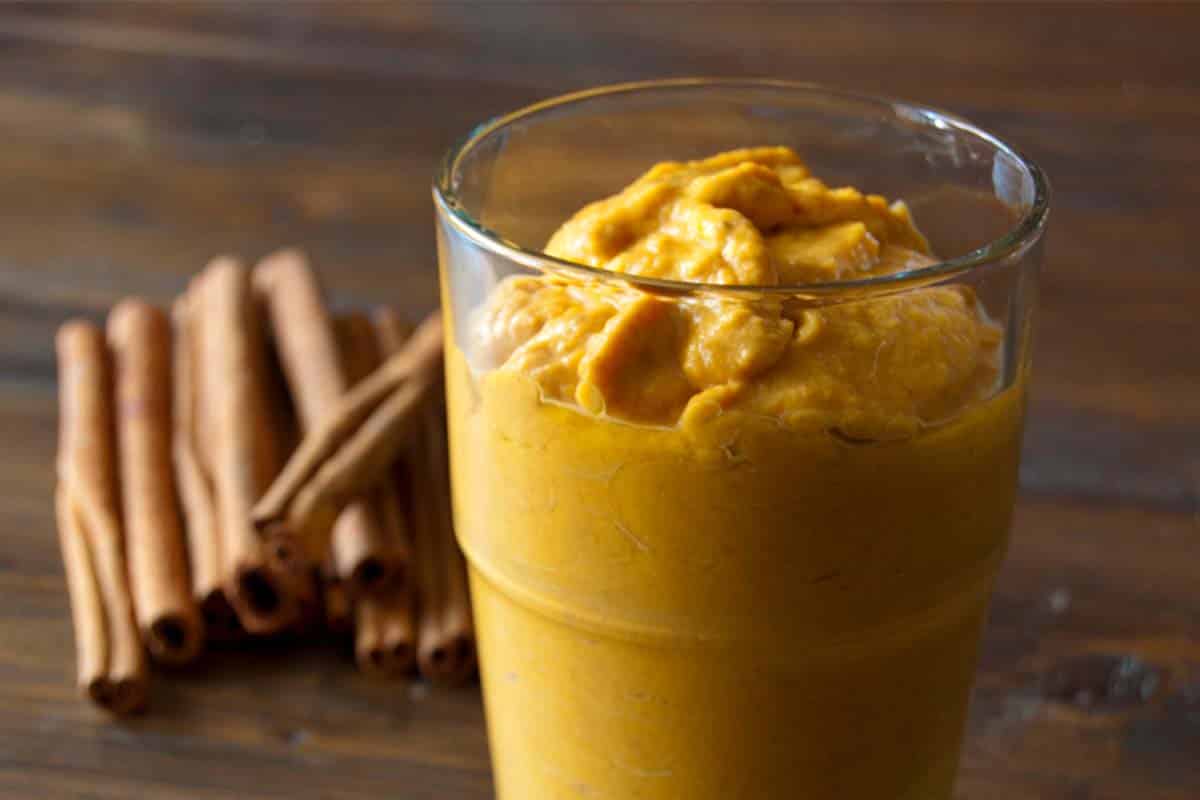 closeup of Pumpkin smoothie in a glass with cinnamon sticks in the background