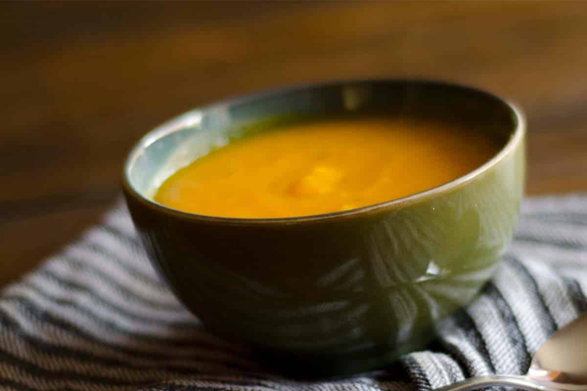 closeup of a green bowl with Pumpkin soup on a wood table