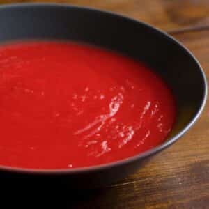 closeup of Red Beet Soup in a black bowl on a wood table