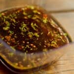 square glass filled with Red Wine Garlic and Thyme Marinade sitting on a wood table