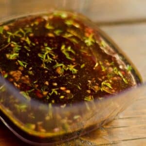 square glass filled with Red Wine Garlic and Thyme Marinade sitting on a wood table