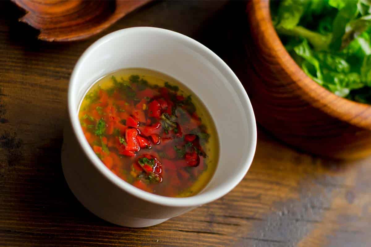 overhead view of Roasted chilli dressing in a ramekin on a wood table with ingredients in the background