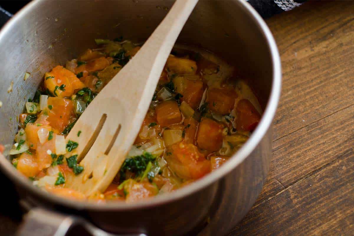 closeup of a pan of Sauce vierge warm dressing with a wooden spoon