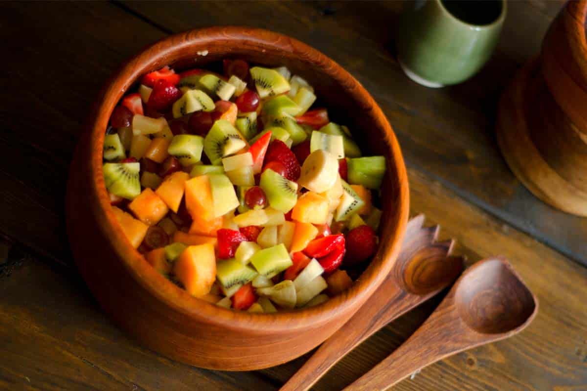 overhead view of a wooden bowl filled with Simple fruit salad on a wood table