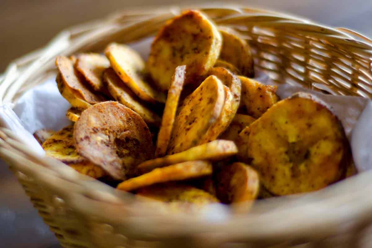 closeup of a basket full of Spicy plantain chips on a wood table