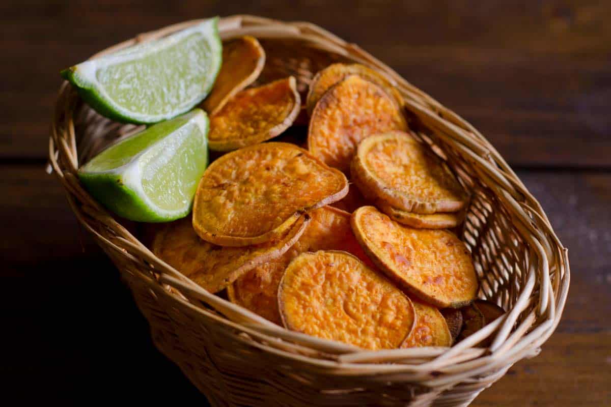 Sweet potato chips and lime slices in a basket on a wood table