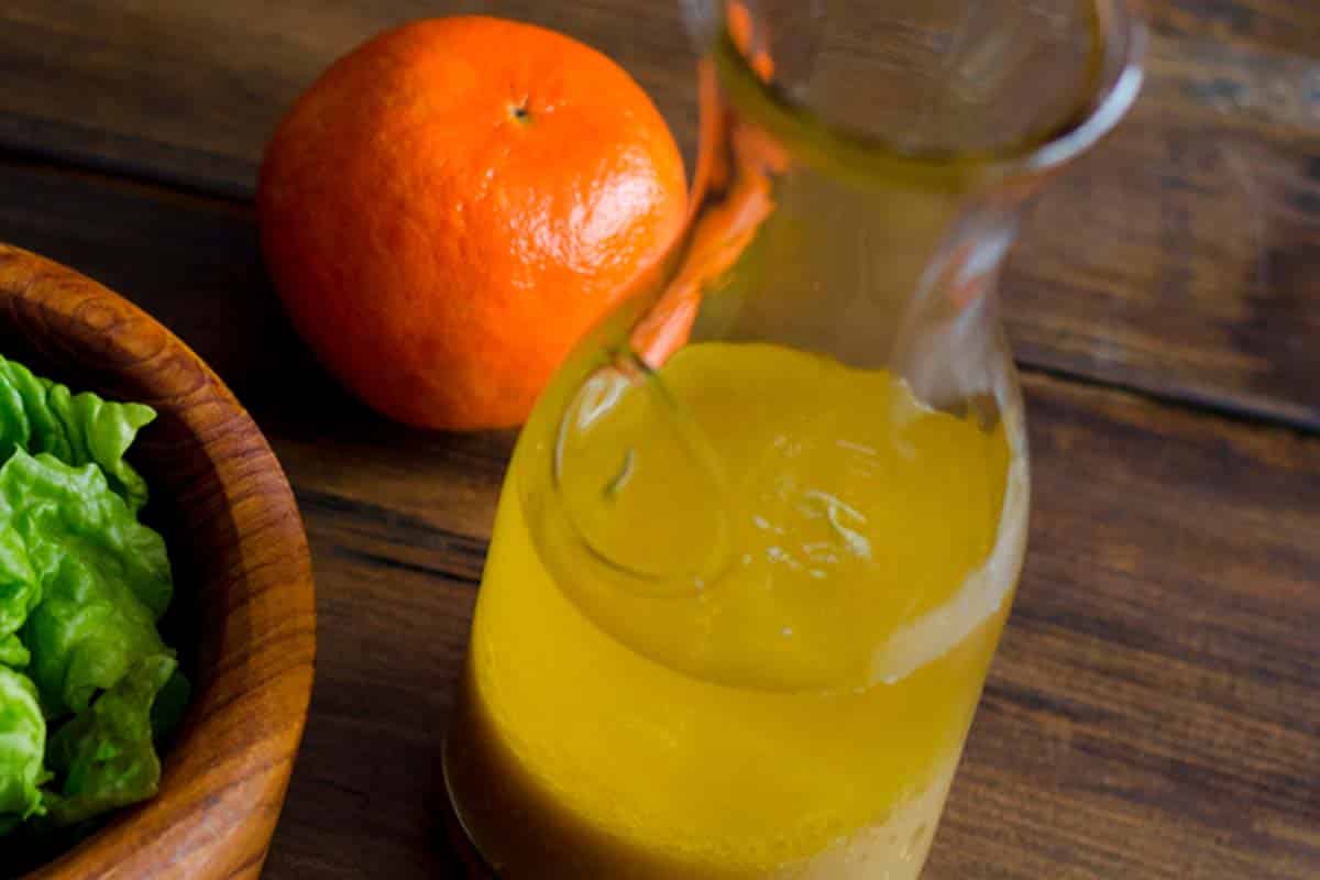 overhead view of Tangerine and pineapple vinaigrette in a glass carafe beside a basic salad and an orange