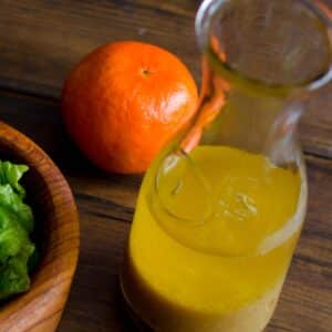 closeup of a glass carafe filled with Tangerine and pineapple vinaigrette on a table next to a mandarin orange