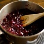 closeup of a wood spoon stirring Tart cranberry sauce in a saucepan