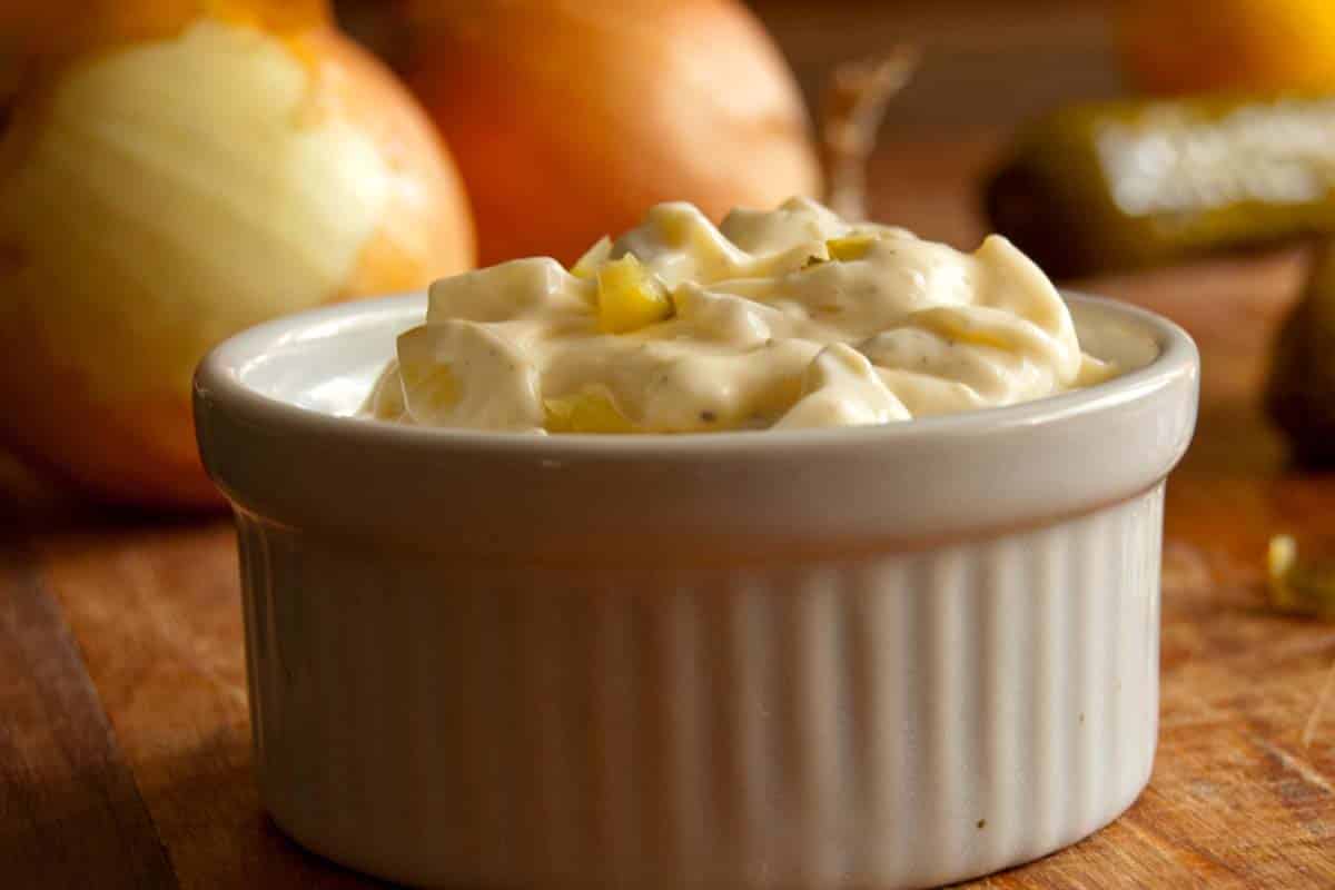 closeup of Tartar Sauce in a ramekin with onions in the background