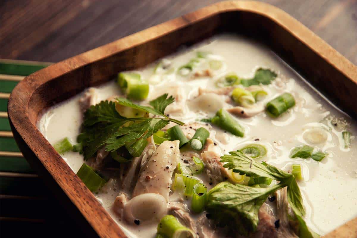 closeup of a square wood bowl filled with Thai chicken soup