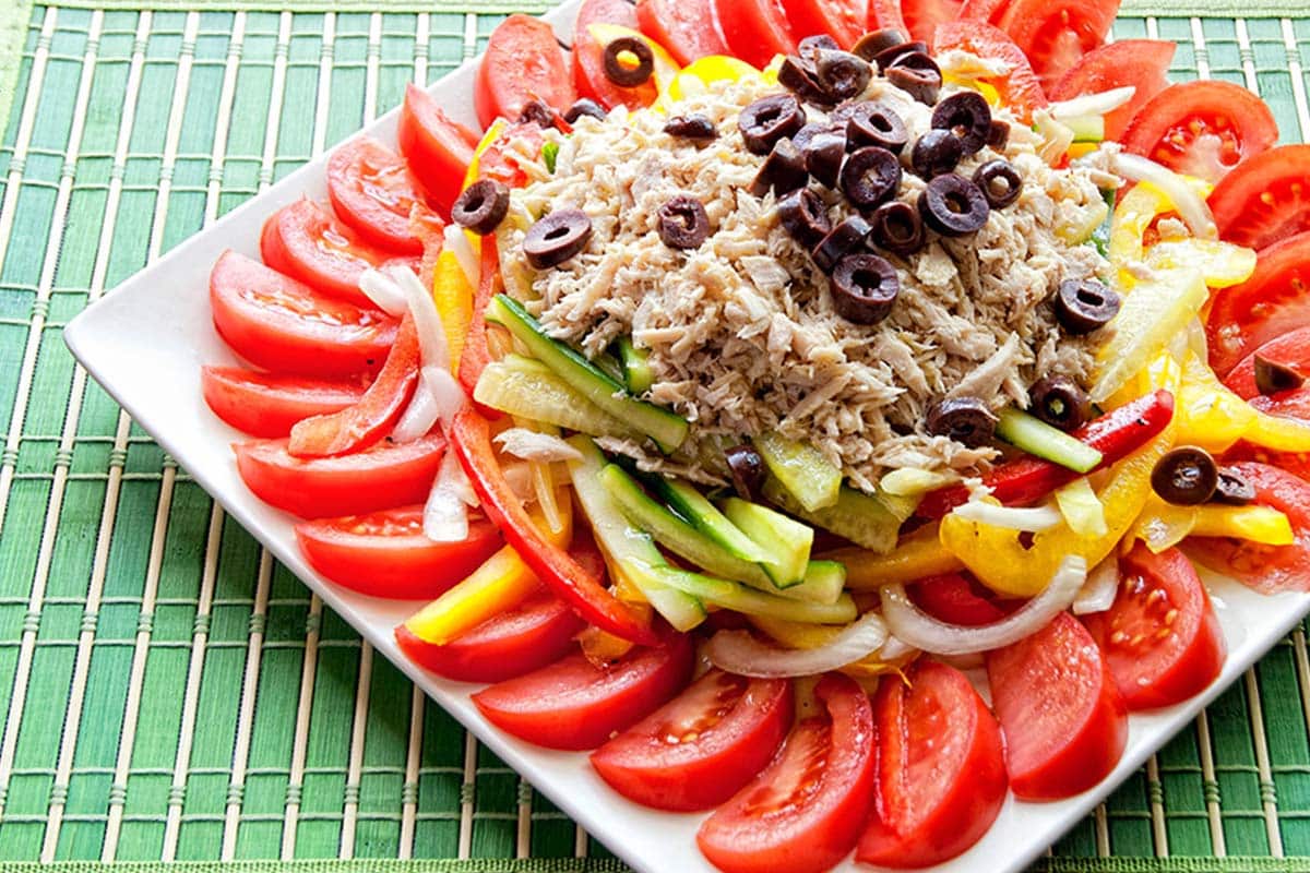 Tuna and summer vegetable salad on a white plate sitting on a green table