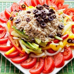 Tuna and summer vegetable salad on a white plate sitting on a green table