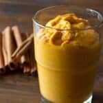 Pumpkin smoothie in a glass on a wood table with cinnamon sticks in the background